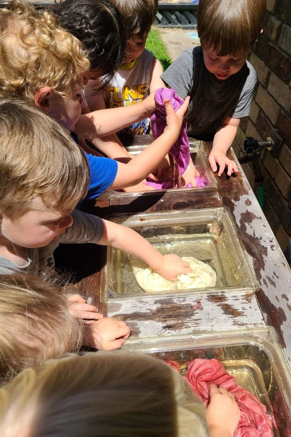 Children washing clothes with natural dyes in shallow tubs of water.