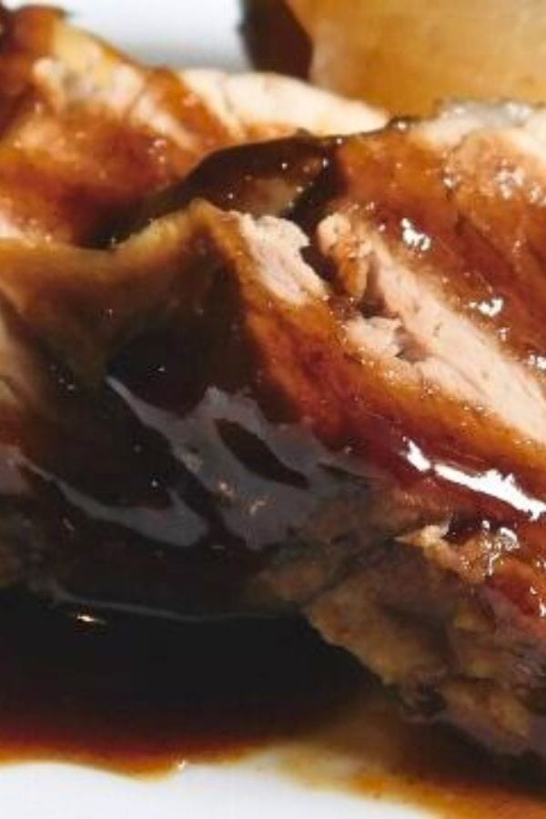 Close-up of a glazed pork roast with a rich brown sauce on a white plate, perfect for crockpot recipes that even satisfy picky eaters.