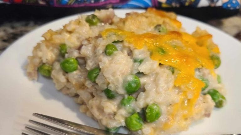A serving of creamy tuna rice casserole with peas, topped with melted cheese, sits invitingly on a white plate, with a fork nearby.