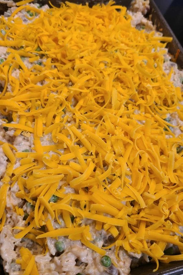 A delectable Tuna Rice Casserole with shredded cheese crowns a savory mixture, featuring visible peas and other delicious ingredients in a baking dish.