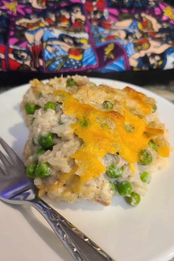 A serving of chicken and rice casserole with peas and melted cheese on a white plate, reminiscent of a classic tuna rice dish, fork beside it; comic book-themed background.
