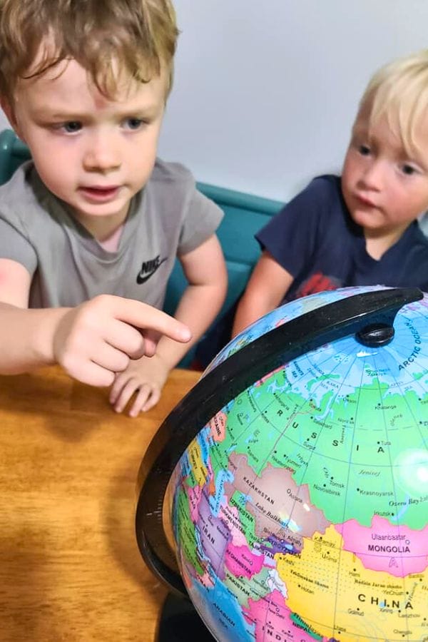 Two boys seated at a table are looking at a globe. One boy points with interest, while the other observes, as they explore lesson plans on French culture.