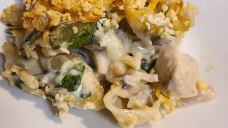A close-up of a pasta dish with chunks of chicken, spinach, and a creamy sauce, topped with a crumbled crispy layer that hints at the savory flair of sour cream and onion tuna.