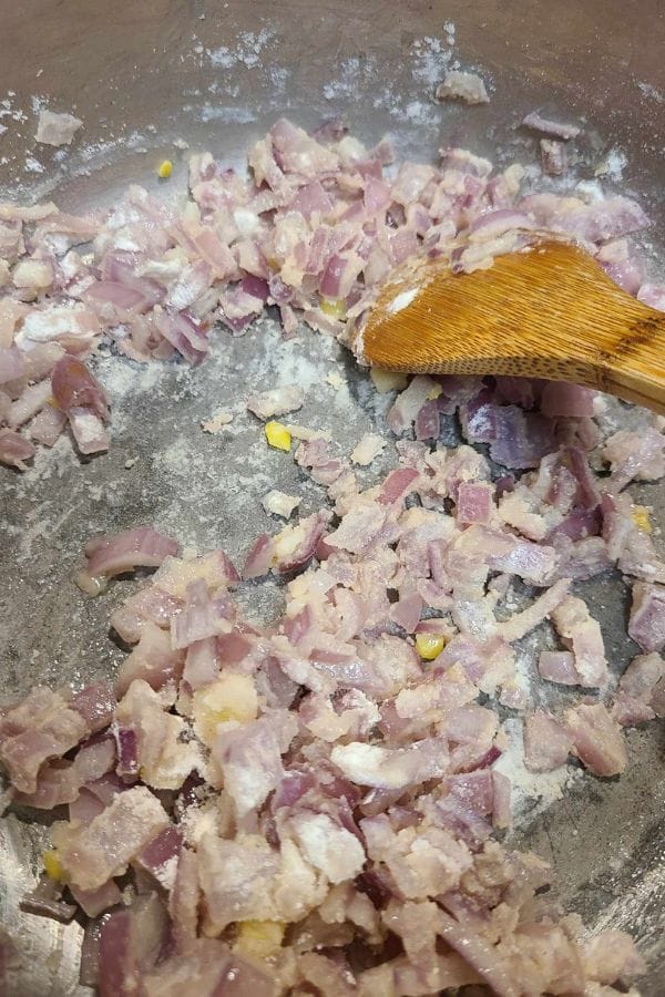 A wooden spatula gently stirs chopped onions in a pan, releasing an aroma reminiscent of sour cream and onion tuna.
