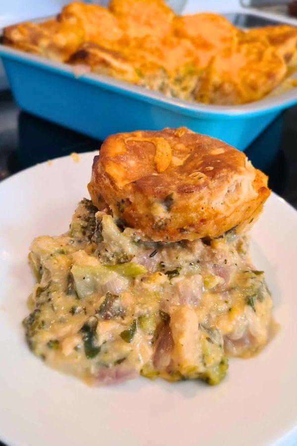 A plate with a creamy broccoli and chicken casserole topped with a golden biscuit, reminiscent of a classic tuna biscuit casserole, with a dish of the casserole in the background.