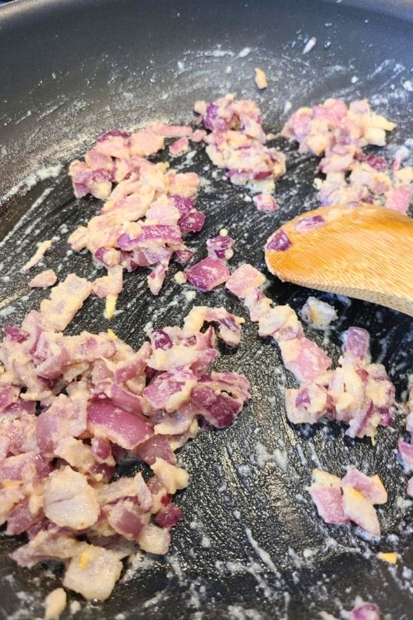 Chopped red onions sautéing in a non-stick pan with a wooden spatula, creating the savory base for a comforting tuna biscuit casserole.