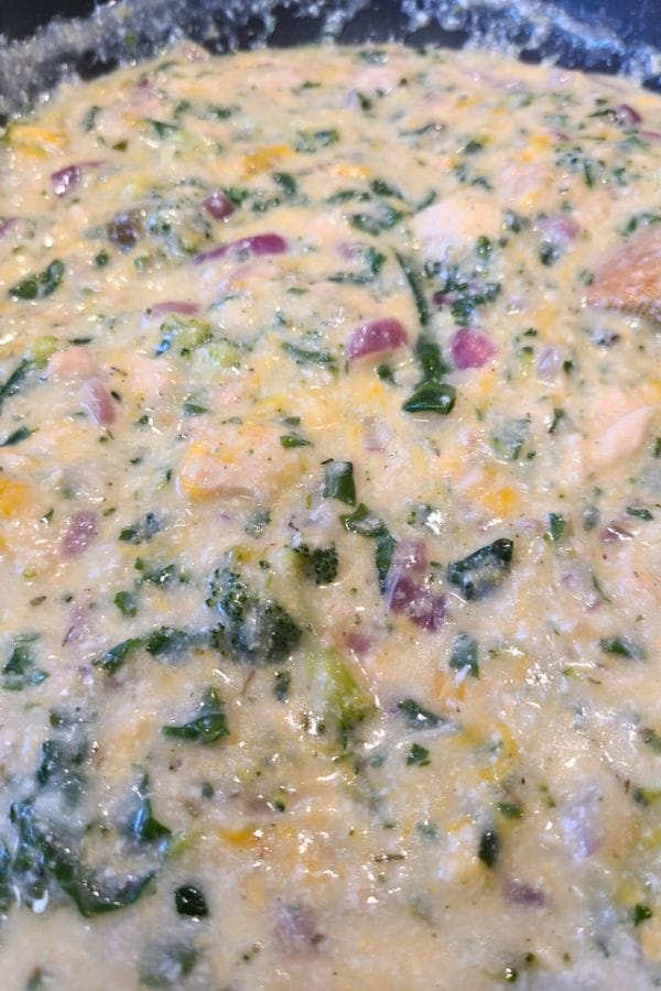 Close-up of a batter mixture with visible chopped spinach, red onions, and melted cheese blended together, reminiscent of a creamy Tuna Biscuit Casserole.