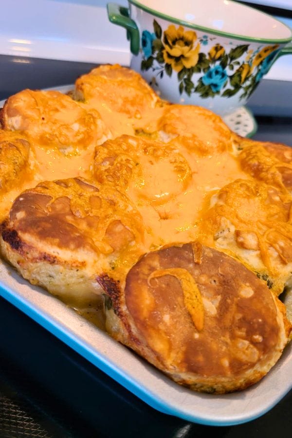 Baked biscuits topped with melted cheese in a tray, featuring a delightful twist of tuna, with a floral teacup in the background.