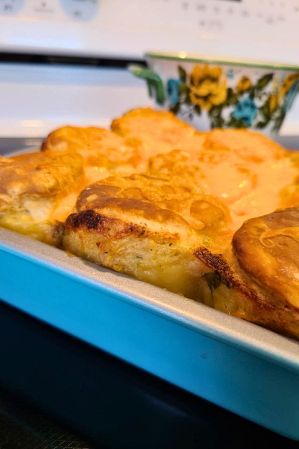 Golden brown tuna biscuit casserole in a blue baking dish, with a floral-patterned bowl in the background on a stovetop.