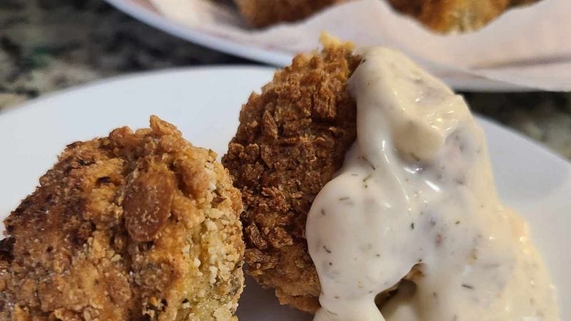 Two fried mushrooms on a plate, one partially covered with a dollop of white sauce, echo the simplicity and delight of easy tuna croquettes.