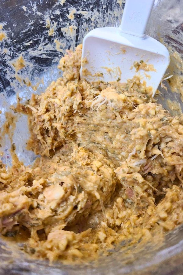 A mixing bowl with a spatula gently stirs a textured, light brown mixture, possibly containing shredded ingredients—perfect for crafting easy tuna croquettes.