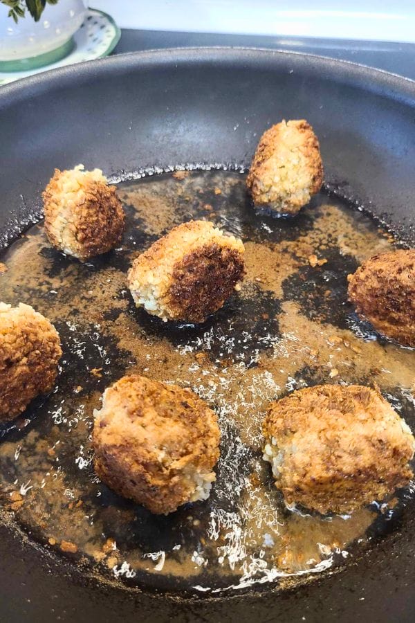 Falafel balls sizzle in a black pan, turning golden brown, similar to how easy tuna croquettes crisp up when perfectly fried.