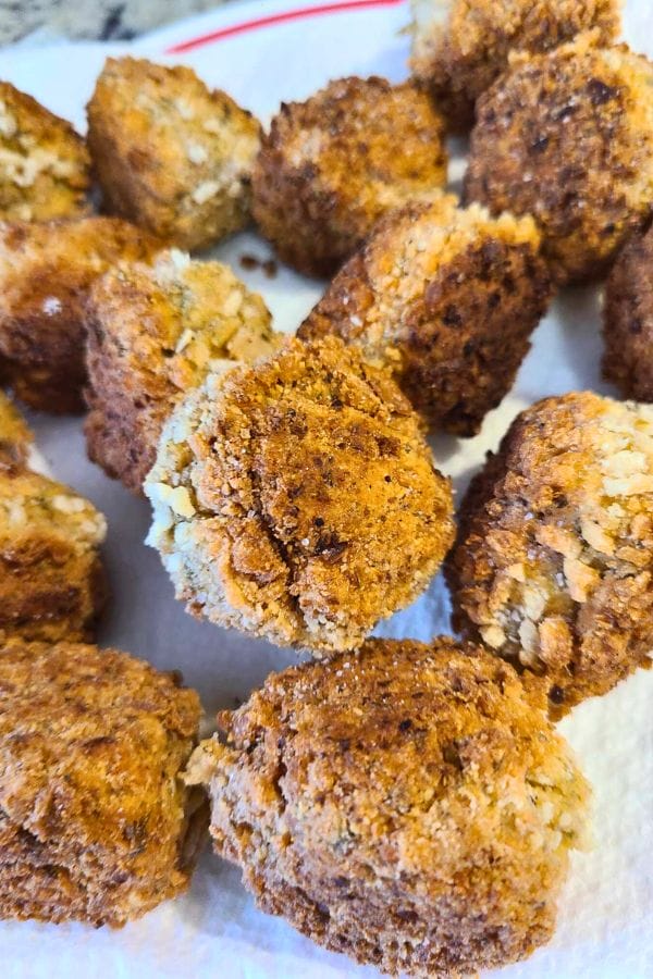 Close-up of several golden-brown fried hush puppies, reminiscent of easy tuna croquettes, resting on a white paper towel.