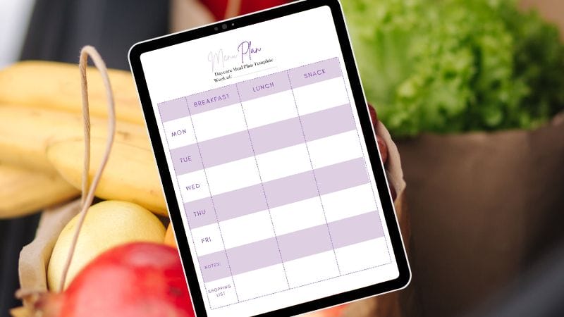A tablet showcasing a daycare meal plan template for the week, with columns for breakfast, lunch, and snack. It rests against a bag of groceries filled with bananas, lettuce, and apples.