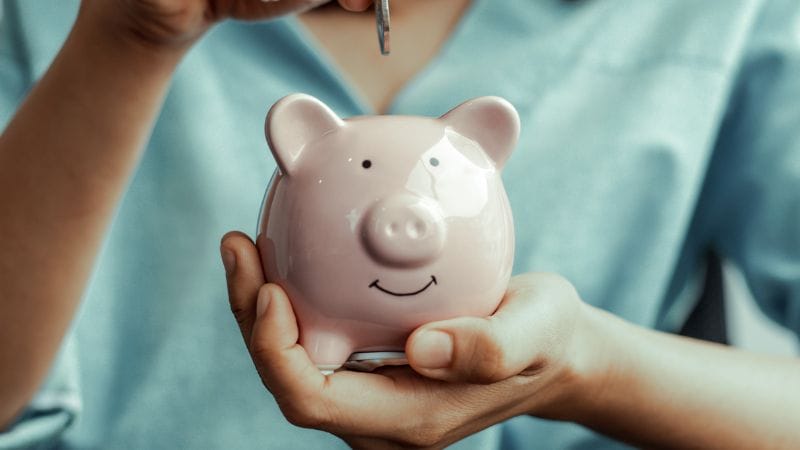A person holding a pink piggy bank with a smiling face illustrates the concept of saving wisely, much like parents do when selecting how to advertise a daycare that ensures their children's future is secure and bright.