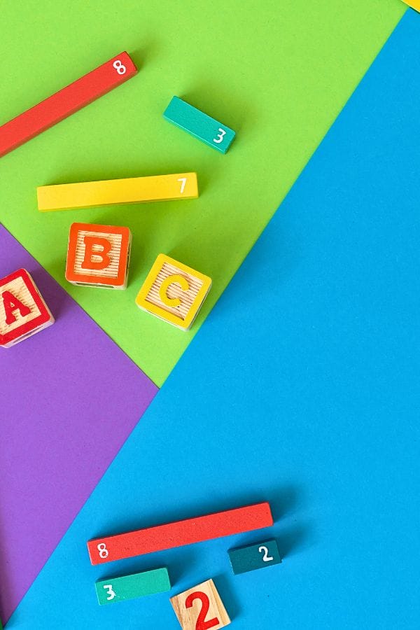 Bright blocks and rods featuring numbers and letters rest on a vibrant geometric paper backdrop, creating a playful scene perfect for illustrating how to advertise a daycare effectively.
