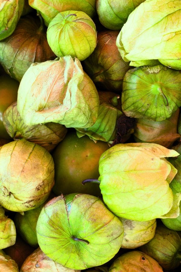 A pile of fresh green tomatillos with paper-like husks partially peeled back, revealing their shiny surfaces—perfect inspiration for those looking to grow tomatillos in containers at home.