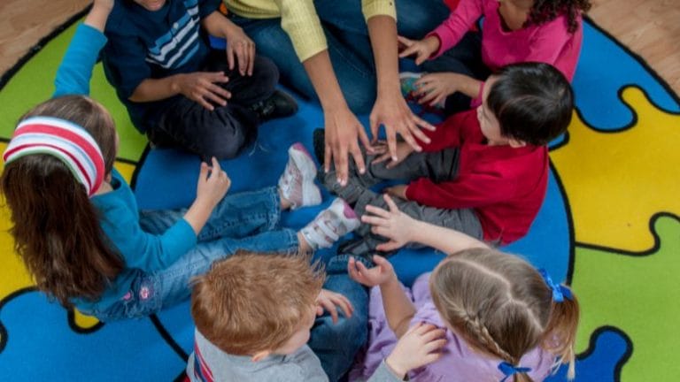 Children sit in a circle on a colorful rug, eagerly engaging in a group activity as an adult leads them through playful tasks, akin to a lively session of interview questions for daycare.