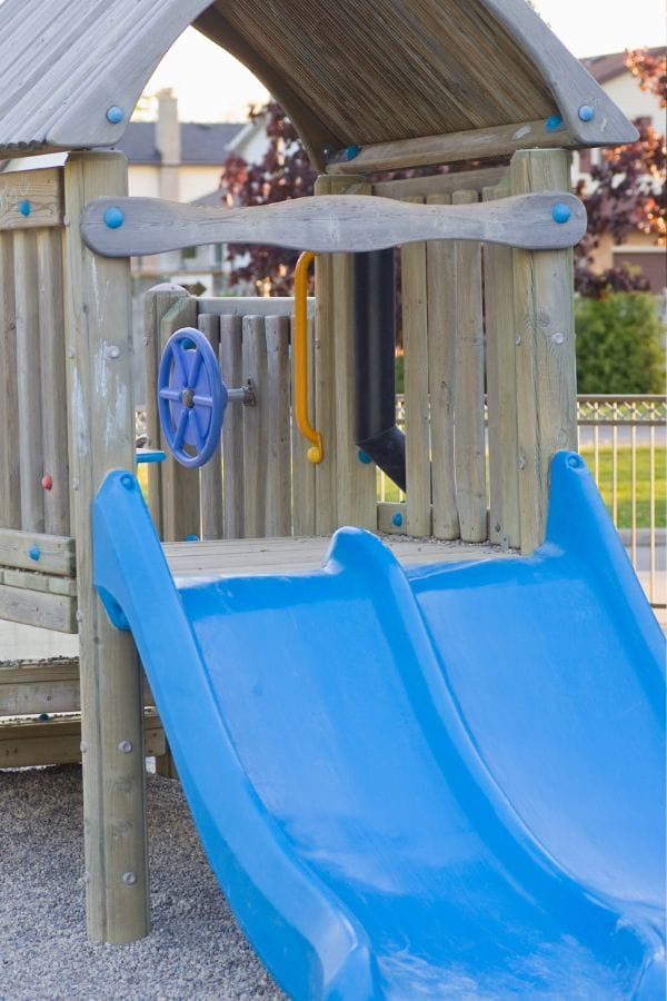 A wooden play structure with a roof, blue slide, and steering wheel serves as the centerpiece of thrilling outdoor playground equipment in an inviting playground setting.