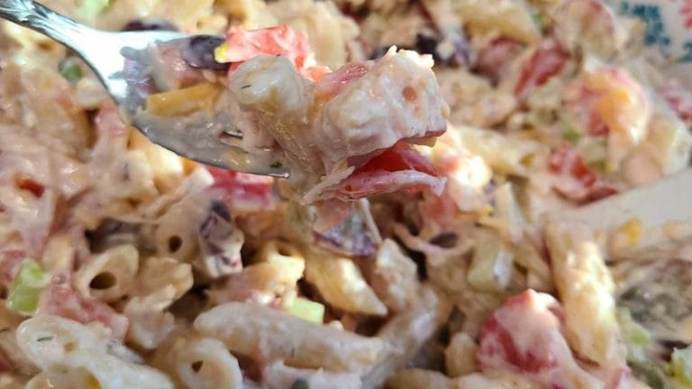 A close-up of a forkful of creamy Ranch Tuna Pasta Salad with penne, diced tomatoes, and chopped vegetables.