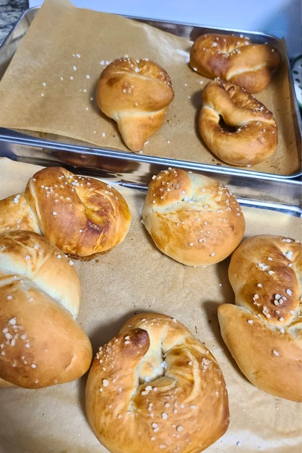 Two baking trays laden with freshly baked pretzels rest on parchment paper, embodying a delicious slice of German culture. The pretzels boast a golden brown crust and are generously sprinkled with coarse salt, inviting you to savor this classic culinary delight.