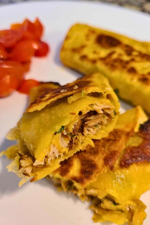 Close-up of a sliced, grilled wrap filled with shredded chicken, resembling easy pork burritos. It's arranged on a white plate with cherry tomato pieces providing a vibrant contrast in the background.