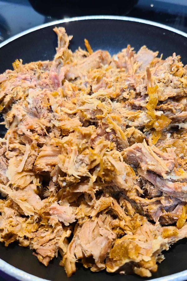 A pan containing cooked, shredded meat with a slightly crispy texture makes for easy pork burritos.