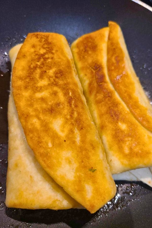 Two golden-brown chimichangas, reminiscent of easy pork burritos, sizzle enticingly in a pan.