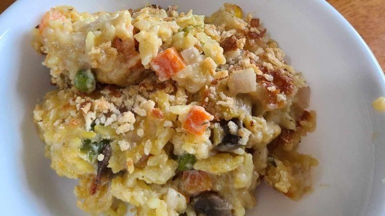 A bowl of creamy leftover pork tenderloin casserole mixed with peas, carrots, mushrooms, rice, and a crispy breadcrumb topping.