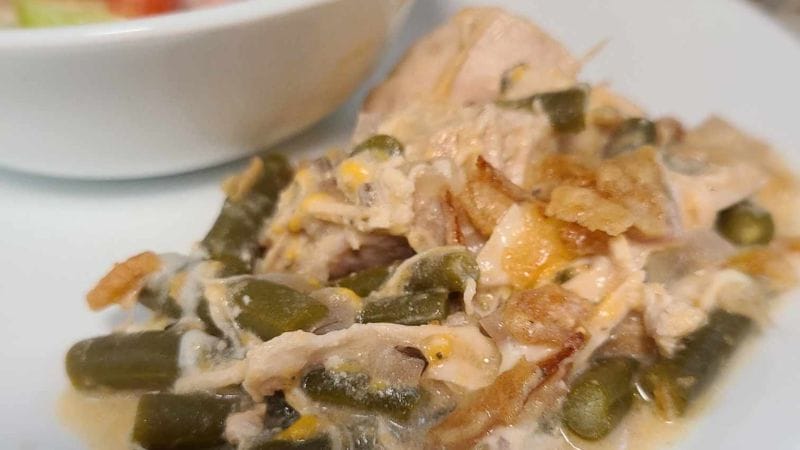 A plate of green bean chicken casserole with crispy onions, creamy sauce, and a side of mixed salad in a bowl.