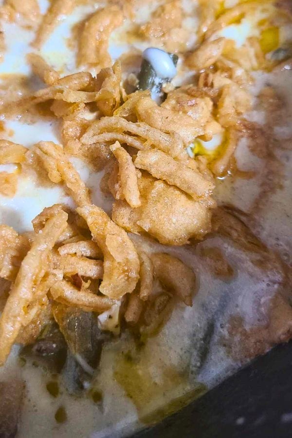A close-up of crispy fried onions crowns a creamy sauce in this Green Bean Chicken Casserole, where bits of mushrooms and vegetables peek through.