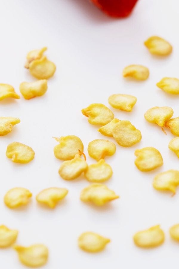 Scattered yellow pepper seeds on a white surface, with part of a fiery red Carolina Reaper visible in the corner.