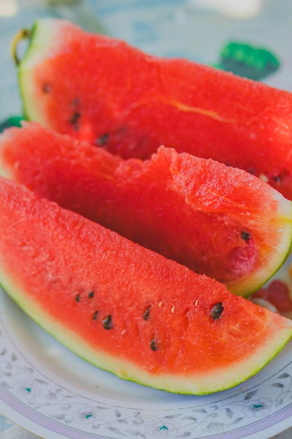 Three slices of watermelon with seeds are artfully arranged on a decorative plate, a delicious reminder of the fruitful rewards when you grow watermelon in a raised bed.
