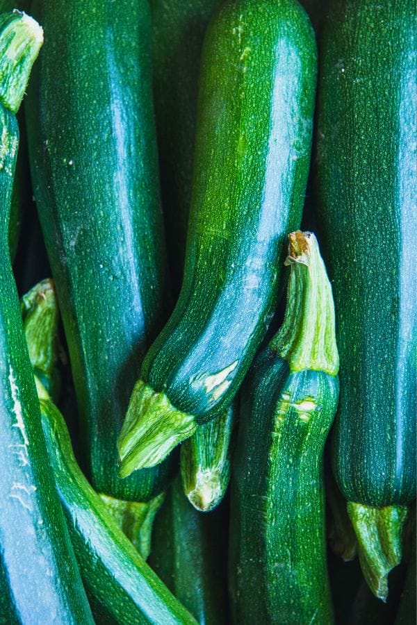 A close-up of several fresh, green zucchinis stacked together, highlighting their smooth texture and vibrant color—a perfect example of the bounty you can enjoy when you grow zucchini vertically.