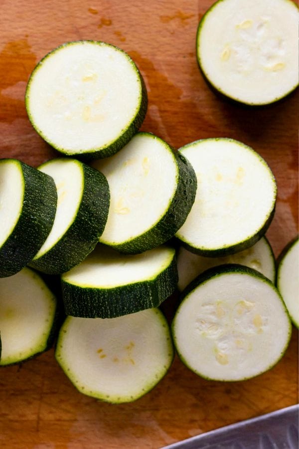 Freshly sliced zucchini lay neatly on a wooden cutting board, perfect for those who choose to grow zucchini vertically in their own garden oasis.