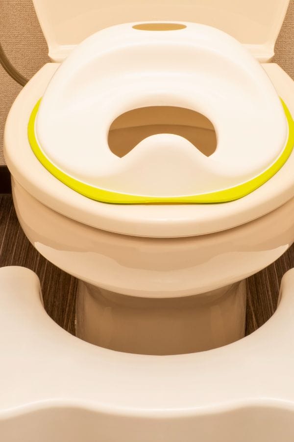 A toilet is shown with a white potty training seat, perfect for those wondering how to potty train. It features a cheerful yellow accent and is accompanied by a white step stool in front of the toilet.