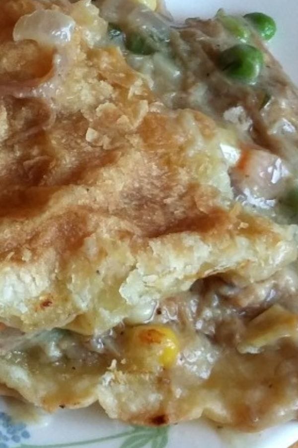 Close-up of a flaky pie crust with a creamy filling of peas, corn, and tender chunks of leftover pork butt mixed with other vegetables on a plate.