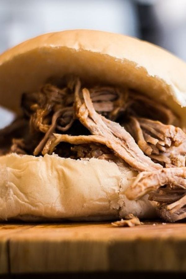 A sandwich with tender shredded meat from leftover pork butt rests invitingly on a wooden surface.