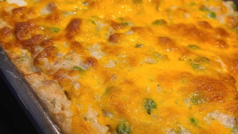 Close-up of a dinner casserole with a golden-brown cheesy top, featuring visible green peas and browned edges in a metal baking dish. Perfect for those who love comforting casserole recipes.