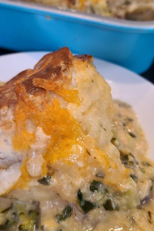Close-up of a savory pie slice on a plate, topped with melted cheese. The pie filling is creamy with visible green vegetables—a delightful take on dinner casserole recipes. A blue baking dish is partially visible in the background.