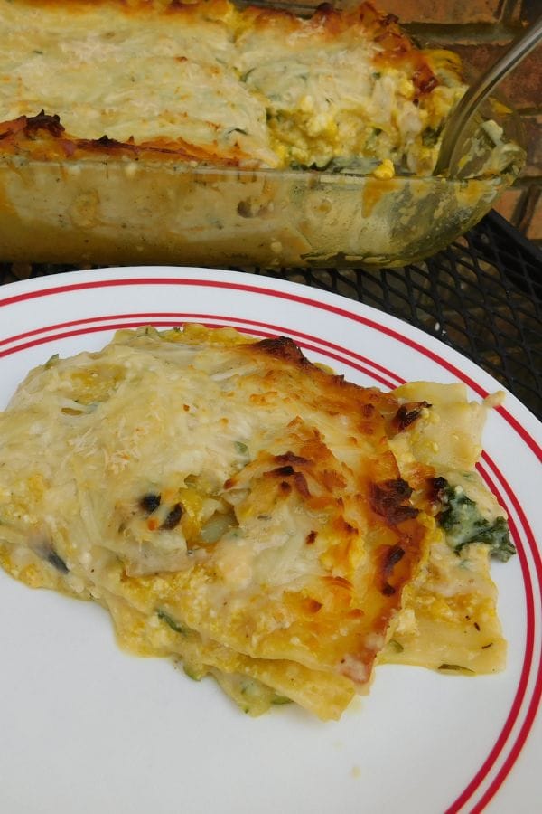 A slice of vegetable lasagna sits on a plate, its golden, melted cheese topping glistening invitingly. In the background, a larger dish teases more of this delicious dinner casserole recipe.