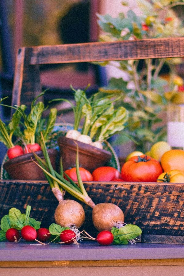 Wooden box containing tomatoes and greens, perfect for those learning to grow food in small spaces. Radishes, spring onions, and turnips are displayed in front.