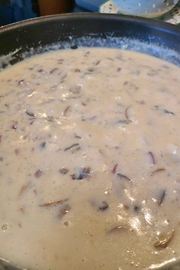 A creamy, rich sauce with chopped onion pieces simmers gently in a black pan, reminiscent of a homemade Cream of Anything Soup.