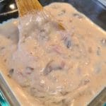 A glass container holds a hearty cream of anything soup, with a wooden spoon expertly stirring the rich, creamy mushroom blend.