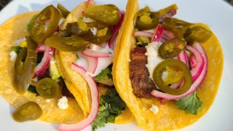 Two leftover brisket tacos with sliced jalapeños, pickled onions, meat, cheese, and cilantro on a plate.