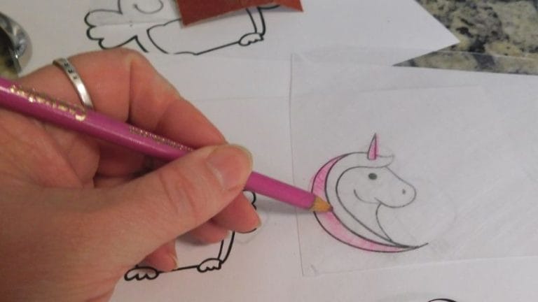 A hand meticulously sketches a unicorn on paper with a pink pencil, reminiscent of Shrinky Dink instructions that transform simple drawings into delightful creations.