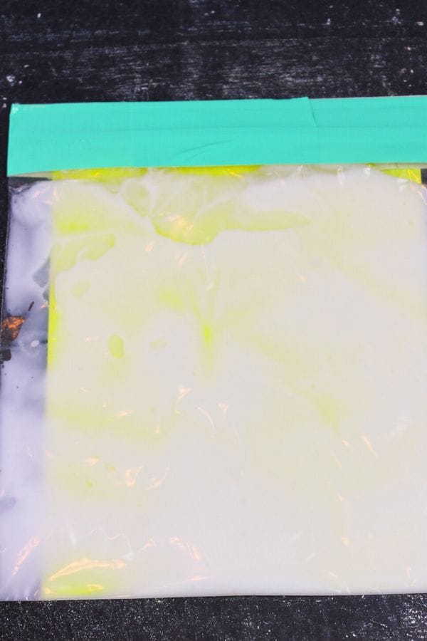 A Glow in the Dark Sensory Bag filled with white liquid is sealed at the top with green tape and placed on a black surface, offering a fun and calming sensory experience.
