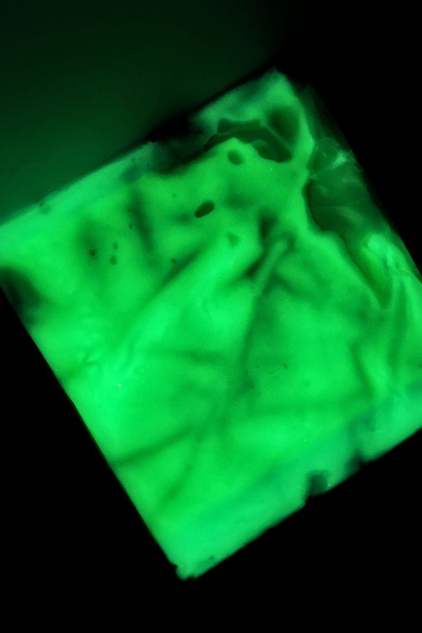 A rectangular Glow in the Dark Sensory Bag glows bright green in the dark, its uneven texture highlighted by ridges and shadows across the surface.
