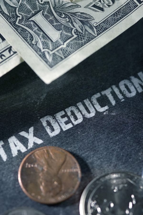 A close-up of U.S. dollar bills and coins on a dark surface with the words "TAX DEDUCTION" partially visible, highlighting the importance of home daycare taxes.