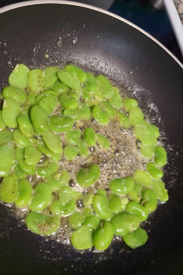 Broad beans, also known as fava beans, are being sautéed in melted butter with bubbles forming and a sprinkle of cracked black pepper—bringing garden-fresh flavor to your kitchen after learning how to grow fava beans.